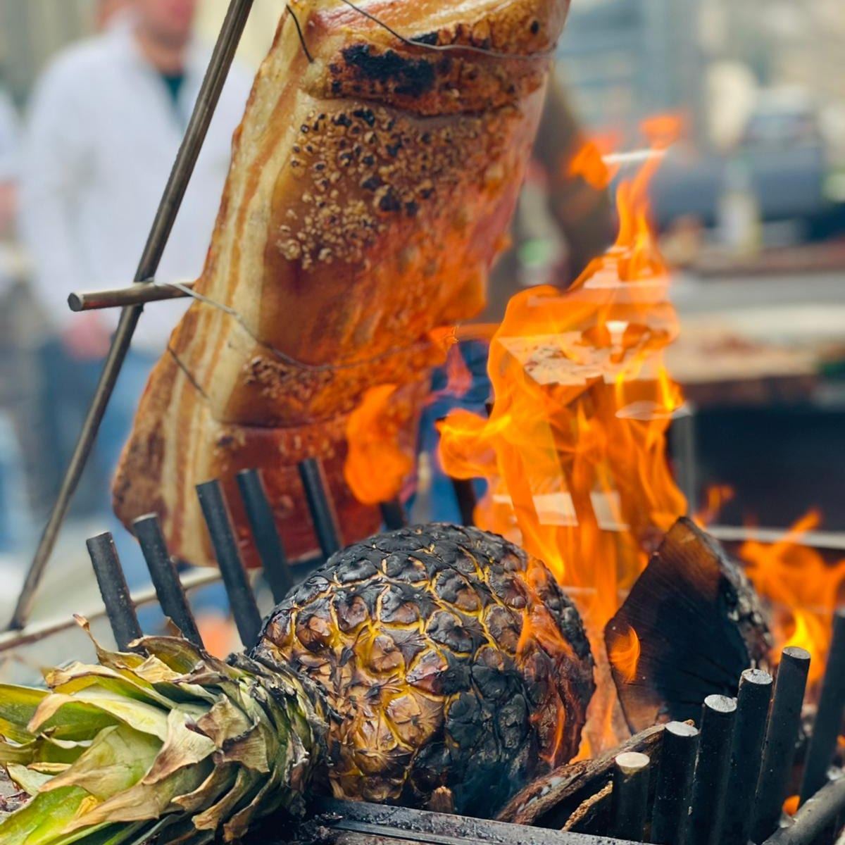 Schweinebauch am Spieß mit offener Flamme und gegrillter Ananas