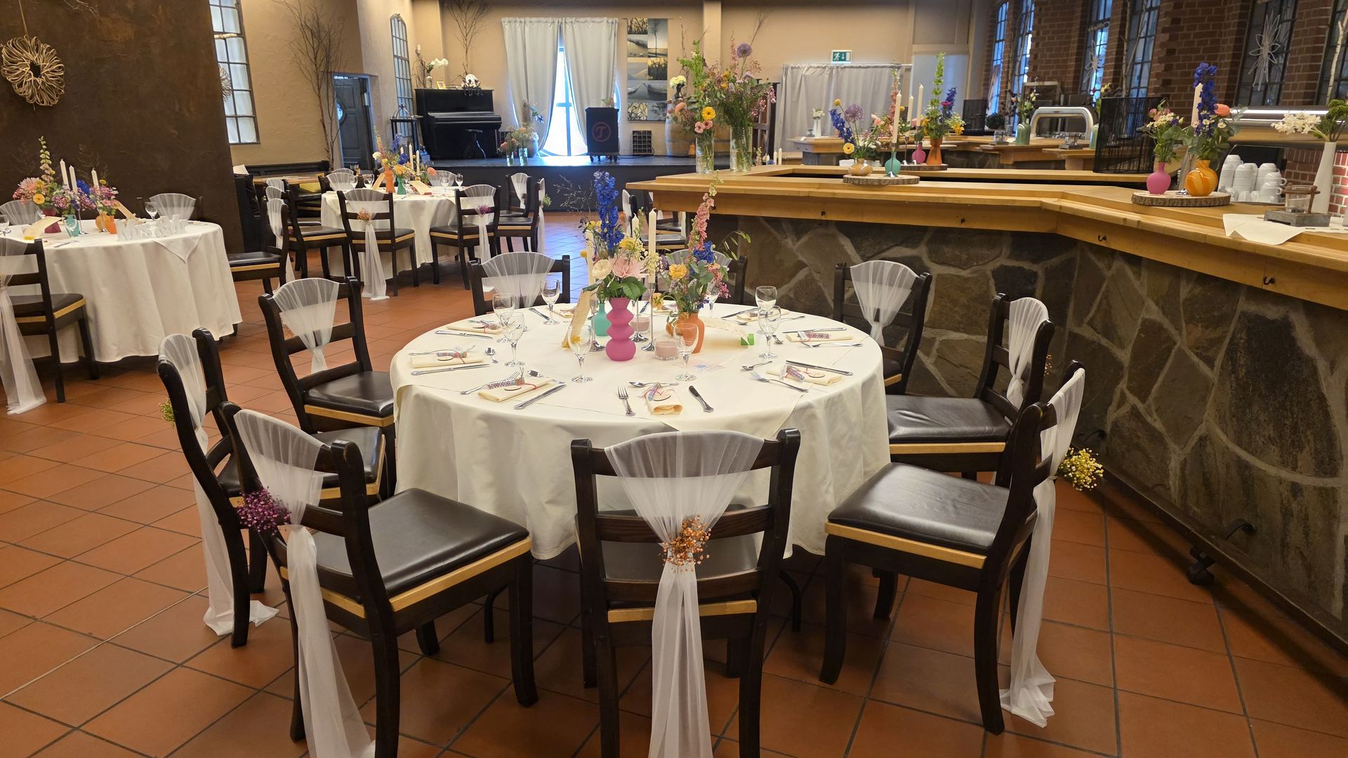Bunt dekorierter Festsaal mit runden Tischen zur Hochzeit